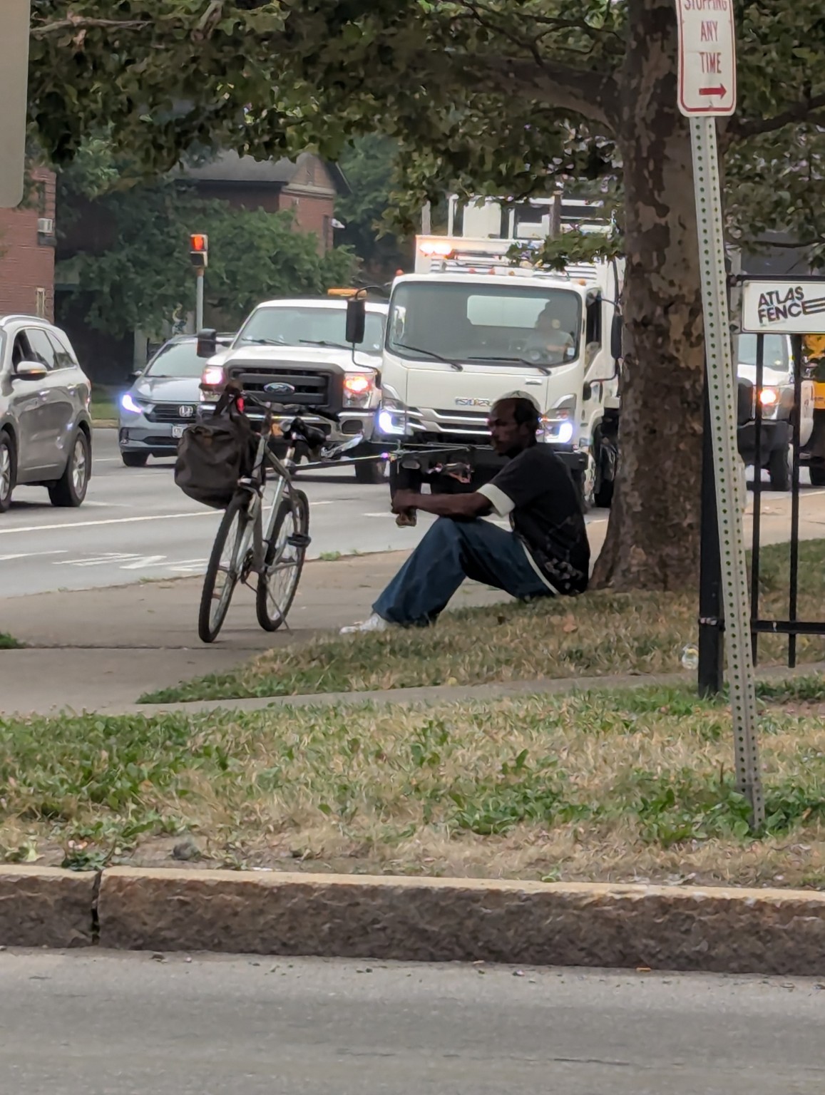 My original street photograph of a seated man beneath a large tree beside his bicycle, with traffic behind him